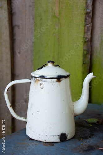Old white vintage enamel teapot on a background of wooden boards.Teapot with chipped enamel,old teapot on a wooden table