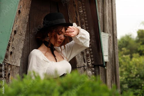 Beautiful woman in vintage dress and hat standing at old wooden door #868739843