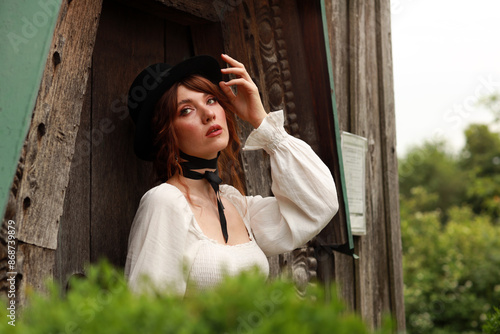 Beautiful woman in vintage dress and hat standing at old wooden door #868739879