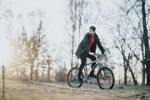 A casual man relishes an afternoon bicycle ride in a park, surrounded by nature and greenery, evoking feelings of relaxation and freedom. Blurred photo.