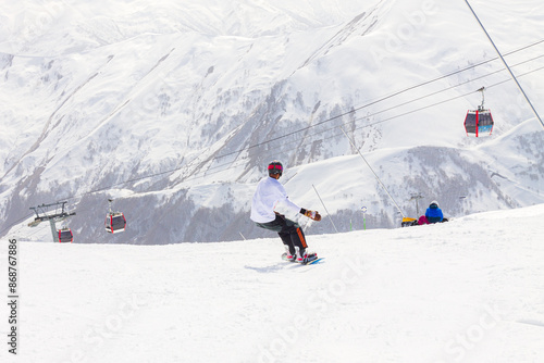 A male snowboarder rides on a snowboard slope on a sunny winter day at the Gudauri ski resort in Georgia