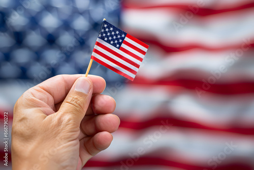 Close-up of a hand holding a small American flag with the United States flag in the background, symbolizing patriotism and national pride photo