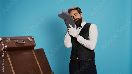 Tired doorman sleeping on pillow in studio, indicating burnout in hospitality industry and feeling exhausted while on duty. Hotel porter employee taking nap after being overworked, sleepy bellhop. photo