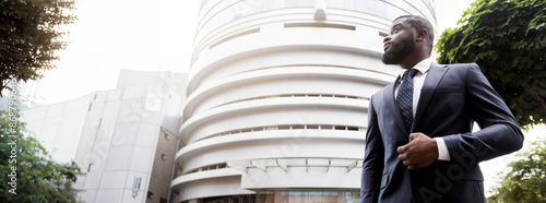 Portrait of thougtful confident black businessman against modern office center background, low-angle shot, panorama with free space photo