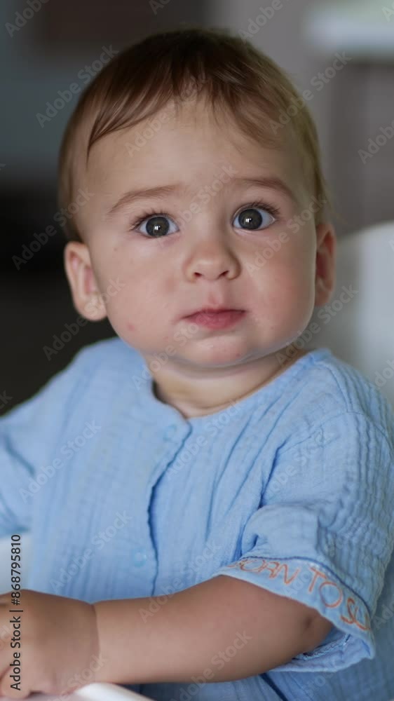 Beautiful little kid sitting calmly at the feeding table. Lovely boy turning around holding a bagel in his hand. Vertical video Beautiful little kid sitting calmly at the feeding table. Lovely boy turning around holding a bagel in his hand. Vertical video