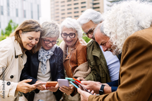 Fotografie Senior group of people using mobile phone device standing in circle outdoors