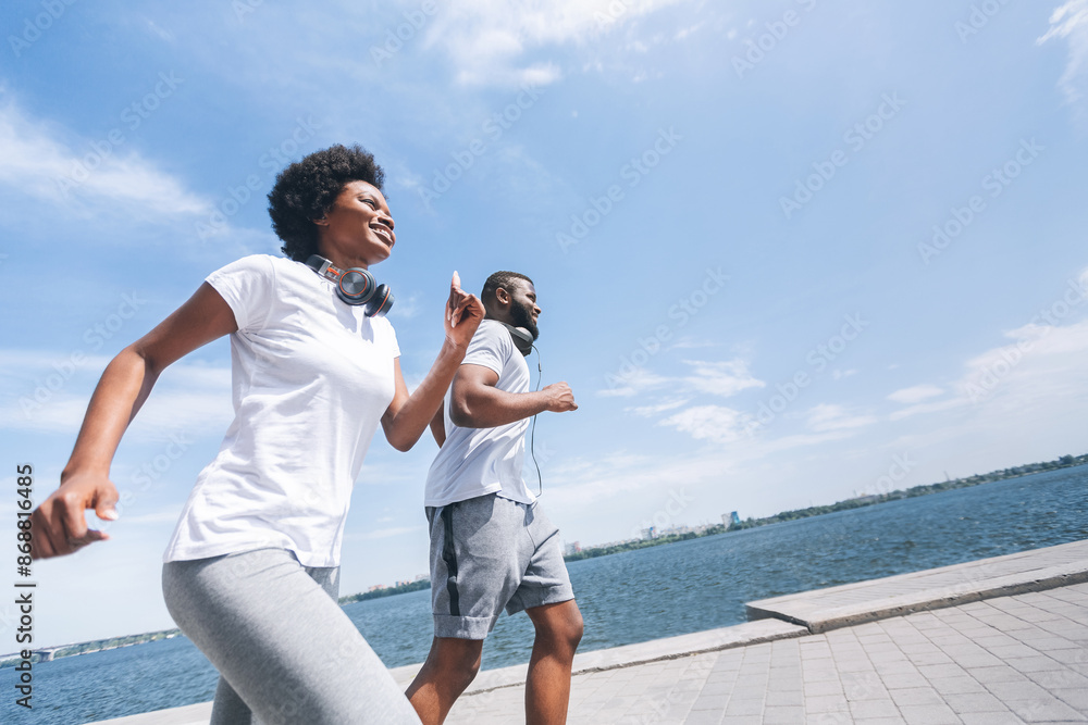 Happy Black Man And Woman Running Near River Bank In City. Jogging In The Morning Free Space, Low-Angle Happy Black Man And Woman Running Near River Bank In City. Jogging In The Morning Free Space, Low-Angle