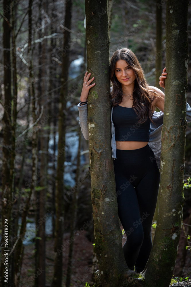 Portrait of a smiling beautiful young woman between two trees in the woods in a bright sunny day Portrait of a smiling beautiful young woman between two trees in the woods in a bright sunny day