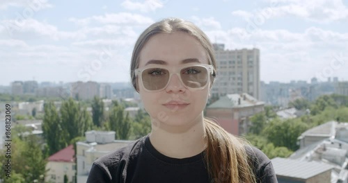 Girl wearing glasses with photochromic lenses. The lenses adjust to changing light conditions, becoming darker in the sun after being transparent indoors. Portrait. Urban city landscape background photo