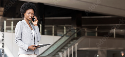 Happy Young African American businesswoman talking on cell phone near office building, free space © Prostock-studio