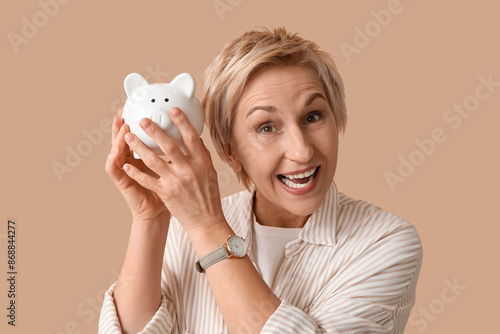 Beautiful mature woman with white piggy bank on brown background