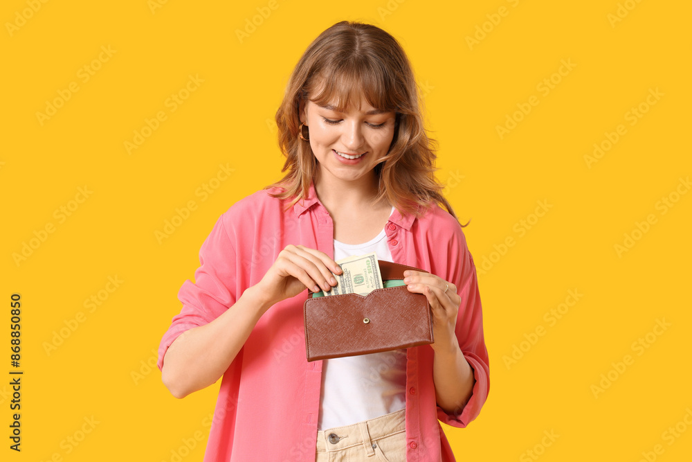 Beautiful young woman holding wallet and money on yellow background Beautiful young woman holding wallet and money on yellow background