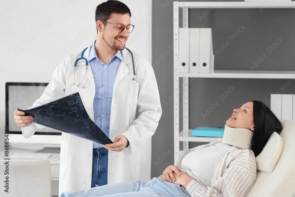 Fototapeta premium Male doctor studying x-ray image of spine with injured woman in clinic