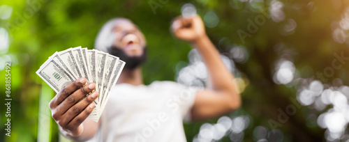 Loterry win. Happy african american man holding fan of dollars in hand outdoor, panorama photo