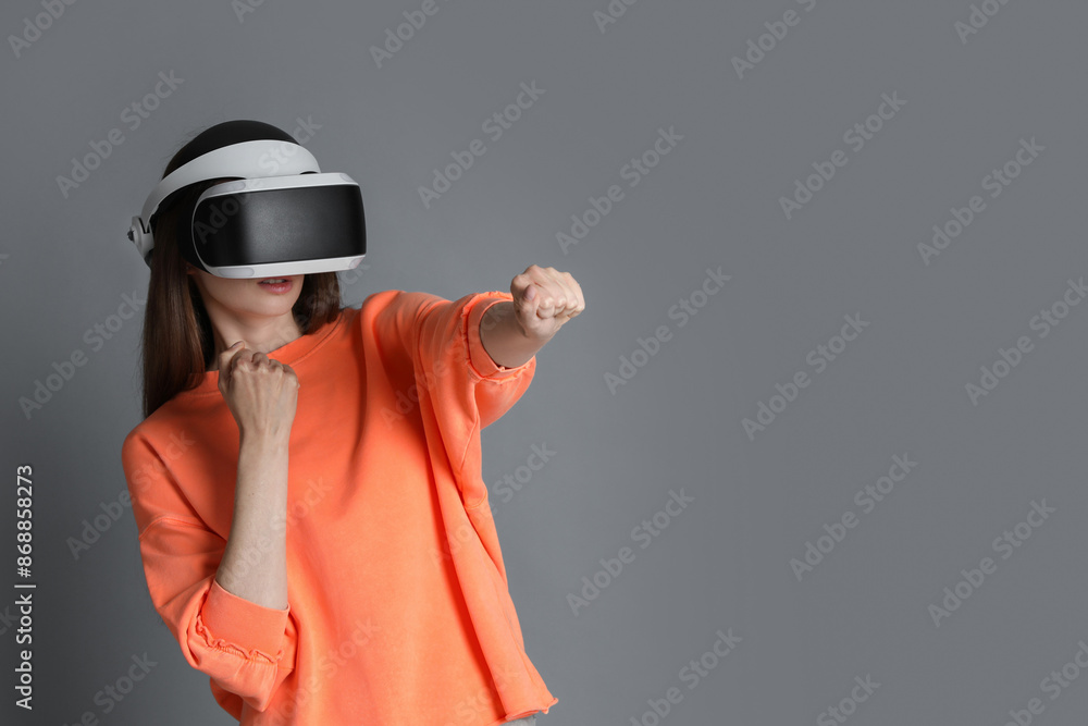 Woman using virtual reality headset on gray background, space for text Woman using virtual reality headset on gray background, space for text