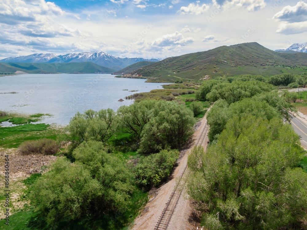 Obraz premium Country road, railway tracks and lake with mountain range in the distance. Midway, Utah, United States of America.