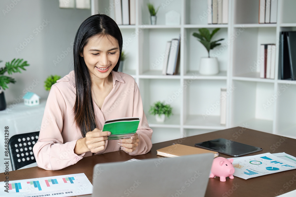 Young Woman Managing Finances at Home with Credit Card, Laptop, and Financial Documents on Desk Young Woman Managing Finances at Home with Credit Card, Laptop, and Financial Documents on Desk
