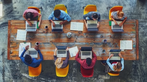 A photo of an office team working together around the table, each with their own laptop and tablet on top of it