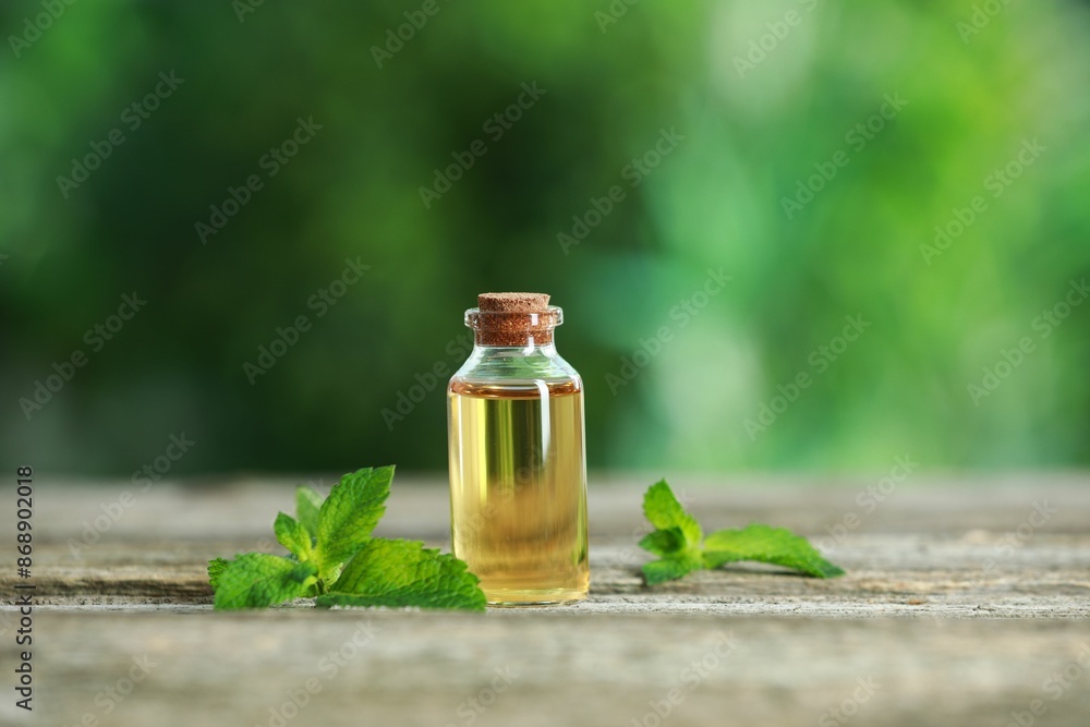 Bottle of mint essential oil and fresh leaves on wooden table Bottle of mint essential oil and fresh leaves on wooden table
