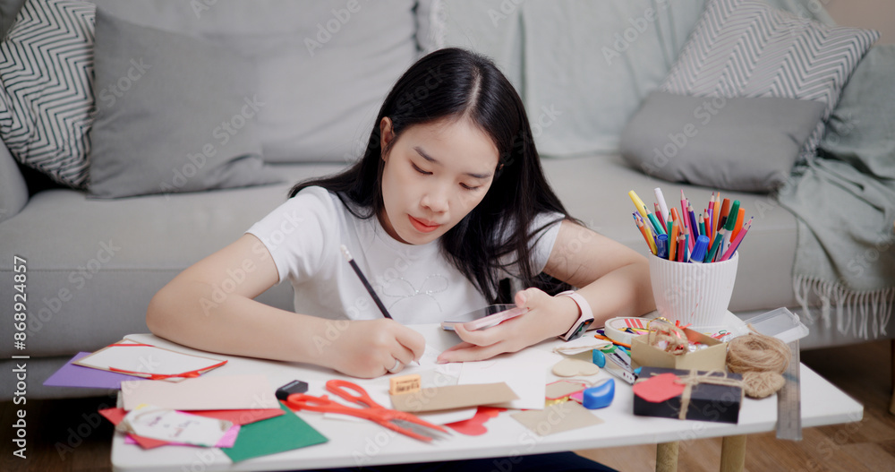 Portrait of Young Asian woman sitting on the floor uses a mobile phone to search for ideas for greeting cards. Holiday hobbies, crafts, DIY cards Portrait of Young Asian woman sitting on the floor uses a mobile phone to search for ideas for greeting cards. Holiday hobbies, crafts, DIY cards