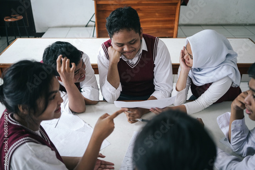 Multiethnic Asian Students Working On School Project While Sitting On Desk And Discussing In The Classroom photo