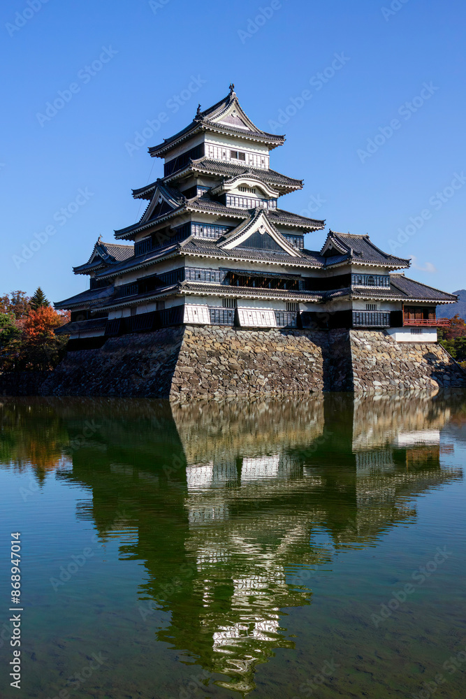Fototapeta premium お堀の水鏡に映る美しい天守閣。 背後には雄大な日本アルプスの山脈が見える。 松本市の象徴、松本城。 日本に5つしかない国宝の城郭である。 市民に広く開放されていて、この位置からは1日中、無料で誰でも撮影することができる。 美しい長野の中核都市、松本市を歩く。 日本国長野県松本市 - 2021年11月7日。