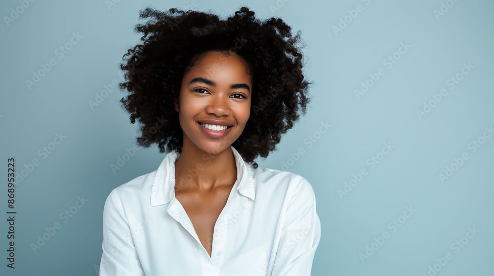 A millennial woman in white, smiling confidently at the camera against a solid light blue background A millennial woman in white, smiling confidently at the camera against a solid light blue background
