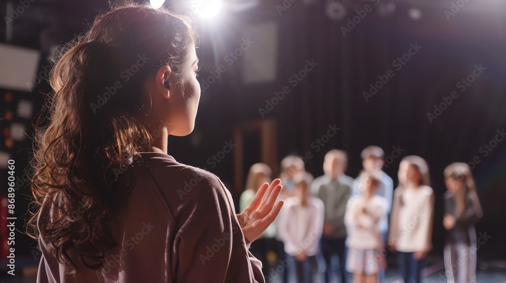 A teacher guides students during a drama class, standing on stage with focus and enthusiasm, under bright stage lights. A teacher guides students during a drama class, standing on stage with focus and enthusiasm, under bright stage lights.