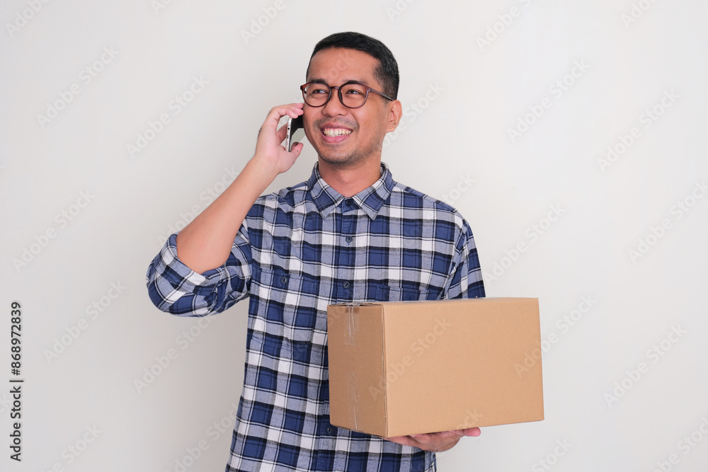 A man holding order package while answering a phone call from his customer. Online business concept A man holding order package while answering a phone call from his customer. Online business concept