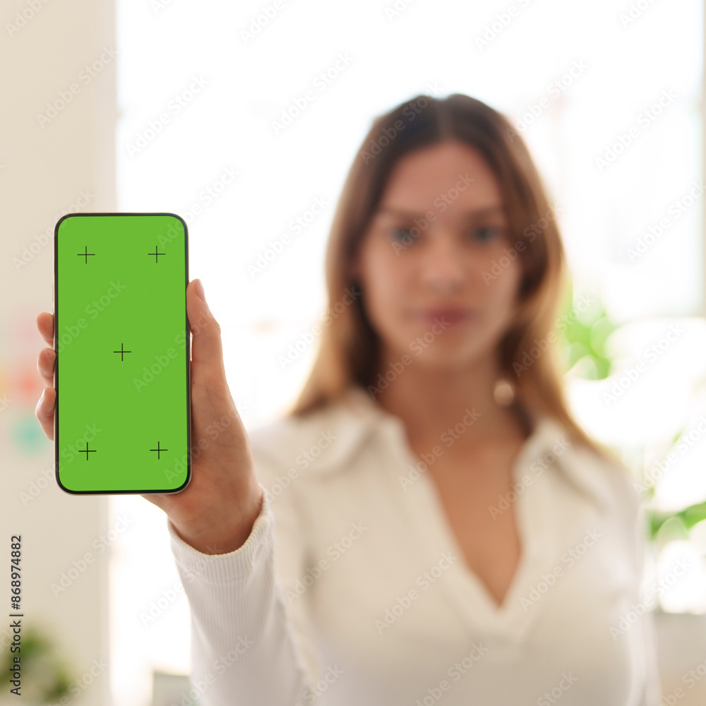 Young woman in office holding mobile phone showing green screen Young woman in office holding mobile phone showing green screen