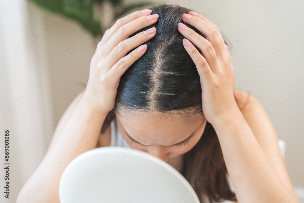 Fototapeta premium Damaged Hair symptom, face serious asian young woman, girl worry about balding, looking at scalp in mirror, hand in break into front hair loss, thin problem. Health care treatment for beauty concept.