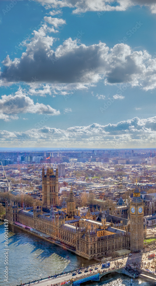 Fototapeta premium Beautiful vertical panoramic view of Westminster Abbey, Big Ben, House of Parliament and the River Thames at sunset with the city of London to the horizon under a sunny sky with backlit white clouds.