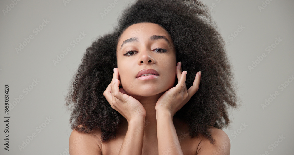 Beauty and healthcare concept - beautiful African American woman with curly afro hairstyle and clean, healthy skin touching face with hand, doing facial massage, posing and looking at camera Beauty and healthcare concept - beautiful African American woman with curly afro hairstyle and clean, healthy skin touching face with hand, doing facial massage, posing and looking at camera