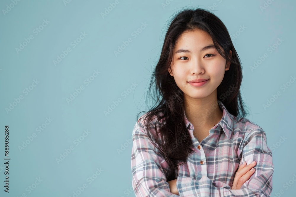 confident smiling young asian woman with crossed arms on light blue background confident smiling young asian woman with crossed arms on light blue background