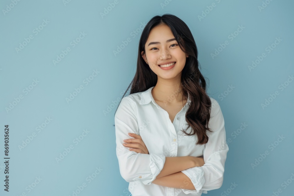 confident smiling young asian woman with crossed arms on light blue background confident smiling young asian woman with crossed arms on light blue background