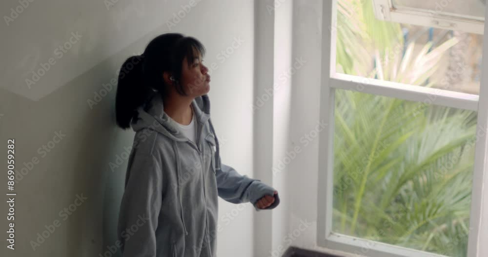 An Asian female high school student was joyfully dancing to music through Bluetooth earphones on her phone while standing by the window after school, secretly reveling in her happy mood. An Asian female high school student was joyfully dancing to music through Bluetooth earphones on her phone while standing by the window after school, secretly reveling in her happy mood.