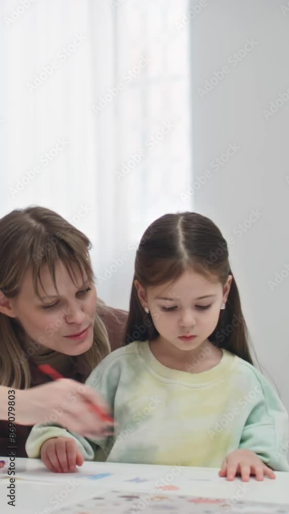 Medium vertical shot of young Caucasian female art teacher supervising young children in drawing lesson in kindergarten, helping individually during process Medium vertical shot of young Caucasian female art teacher supervising young children in drawing lesson in kindergarten, helping individually during process