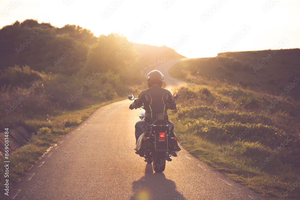Biker driving a motorcycle rides along the asphalt road in sunset. Biker driving a motorcycle rides along the asphalt road in sunset.