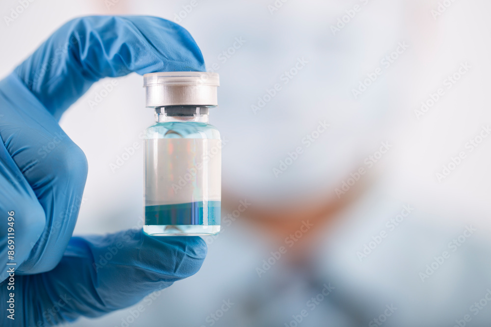 A gloved hand holds a small vial of clear liquid, representing healthcare and medical treatments. A gloved hand holds a small vial of clear liquid, representing healthcare and medical treatments.