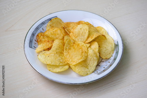 Potato chips on a white plate on wooden background. Crunchy delicious lays potato chips, American style cream and onion flavor.