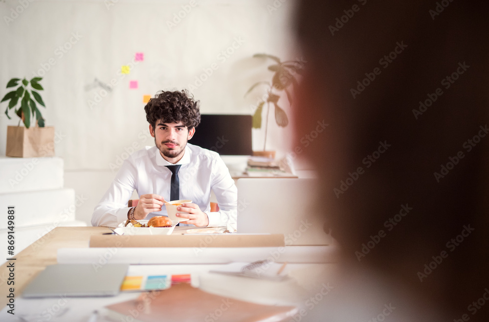 Fototapeta premium Businessman having quick lunch, fastfood meal in startup company office. Working in co-working space.