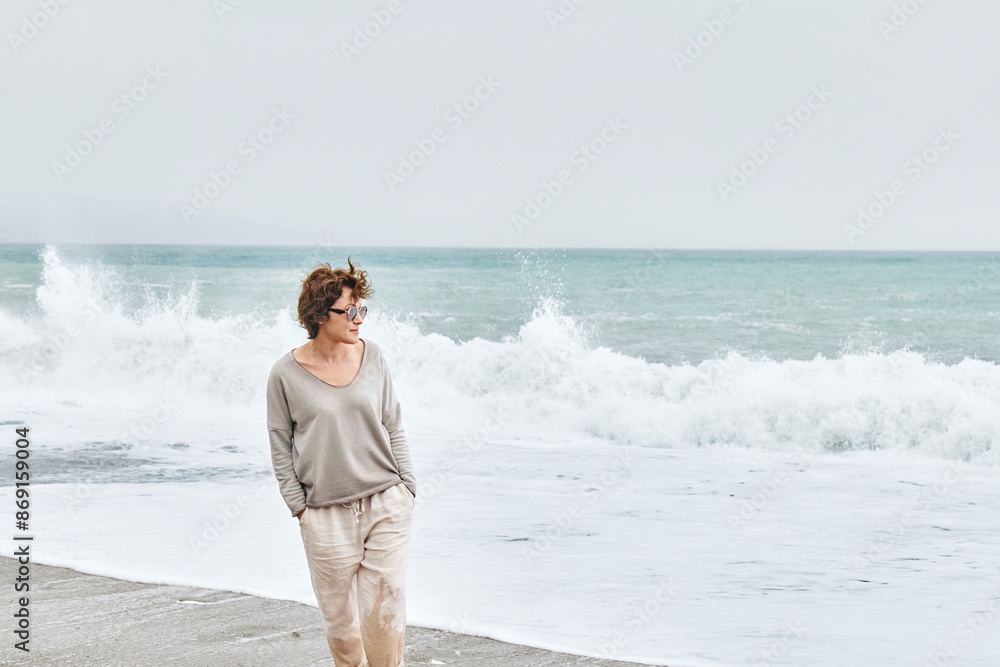 Woman walking along coastline with hands in pockets at beach Woman walking along coastline with hands in pockets at beach