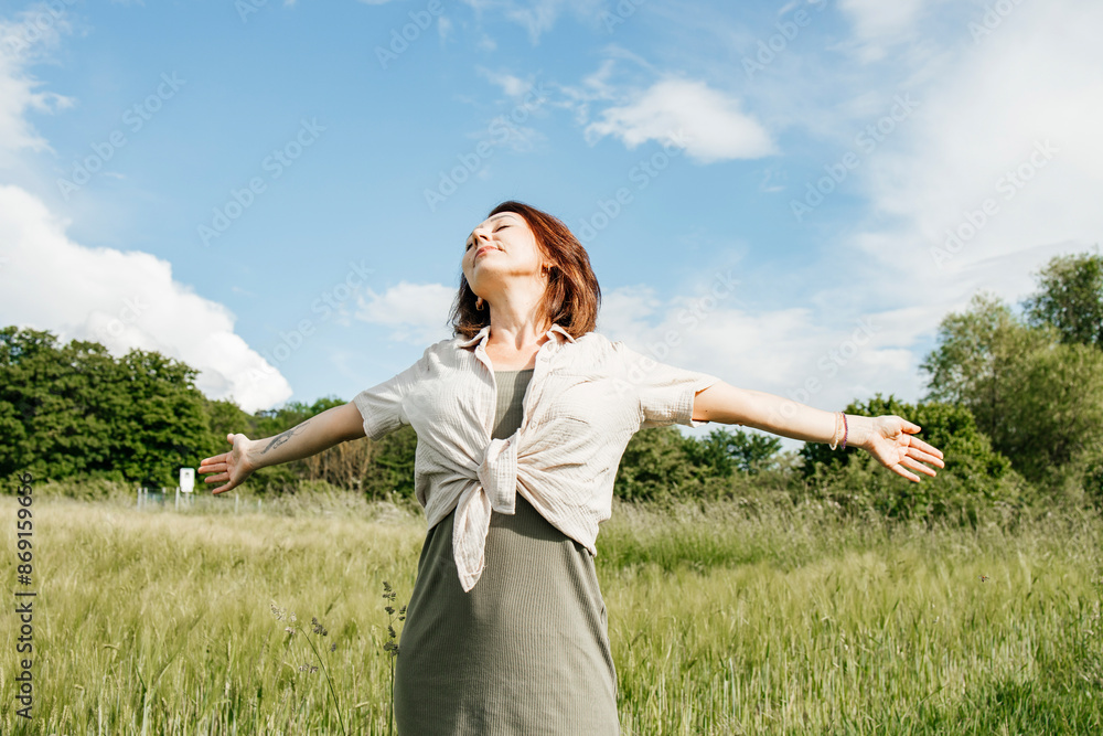 Happy woman with arms outstretched standing on field under cloudy sky