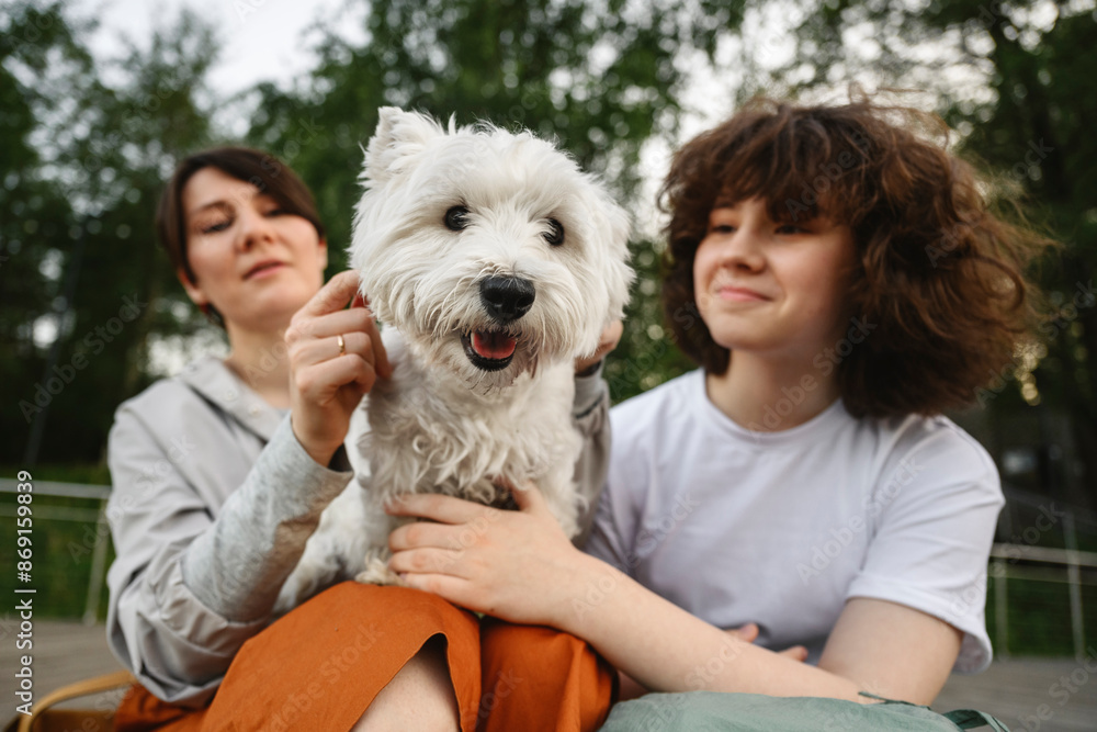 Mother and daughter petting white dog Mother and daughter petting white dog