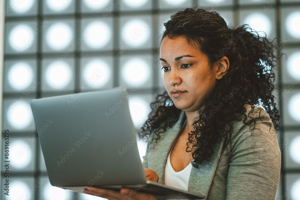 Businesswoman using laptop and standing near illuminated wall at office Businesswoman using laptop and standing near illuminated wall at office