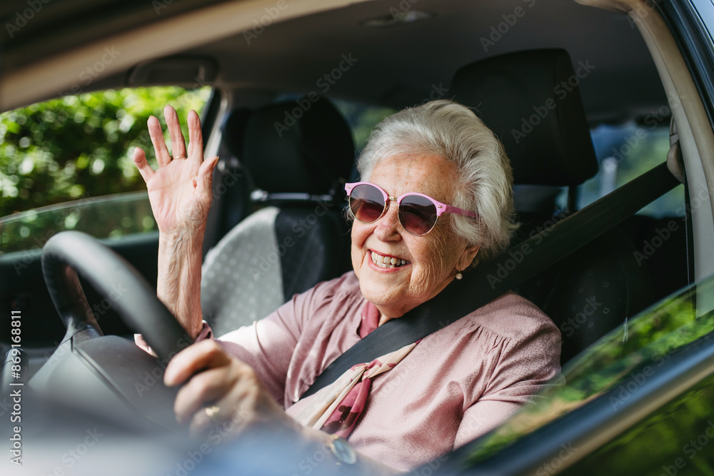 Obraz premium Happy senior woman driving car alone, enjoying car ride. Safe driving for elderly adults, older driver safety.