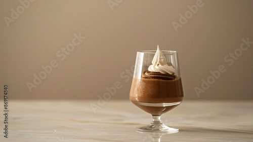 A minimalist dessert presentation of a small chocolate mousse, served in a clear glass with a tiny dollop of whipped cream on top photo