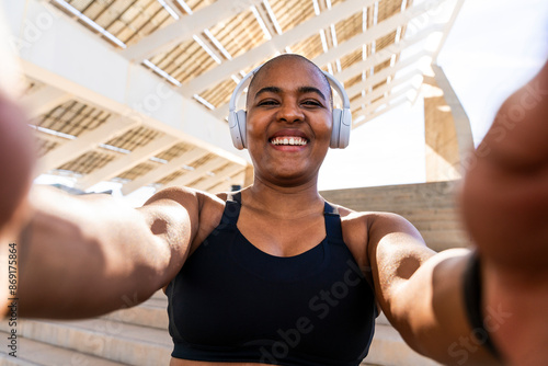 Happy sporty woman wearing headphones taking selfie on sunny day