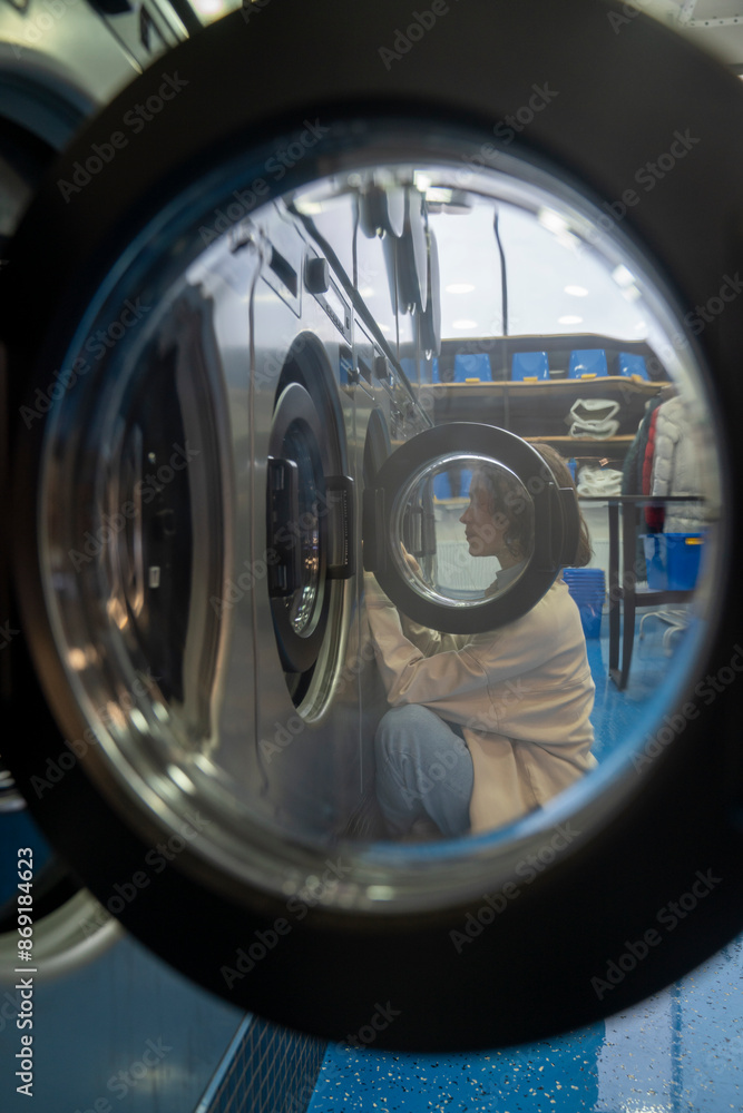 Young woman seen through washing machine open glass in laundromat Young woman seen through washing machine open glass in laundromat