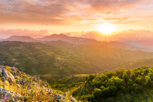 highland mountain landscape of beautiful sunset or sunrise with nice mountain peaks and slopes, green and golden hills and majestic cloudy sky on background